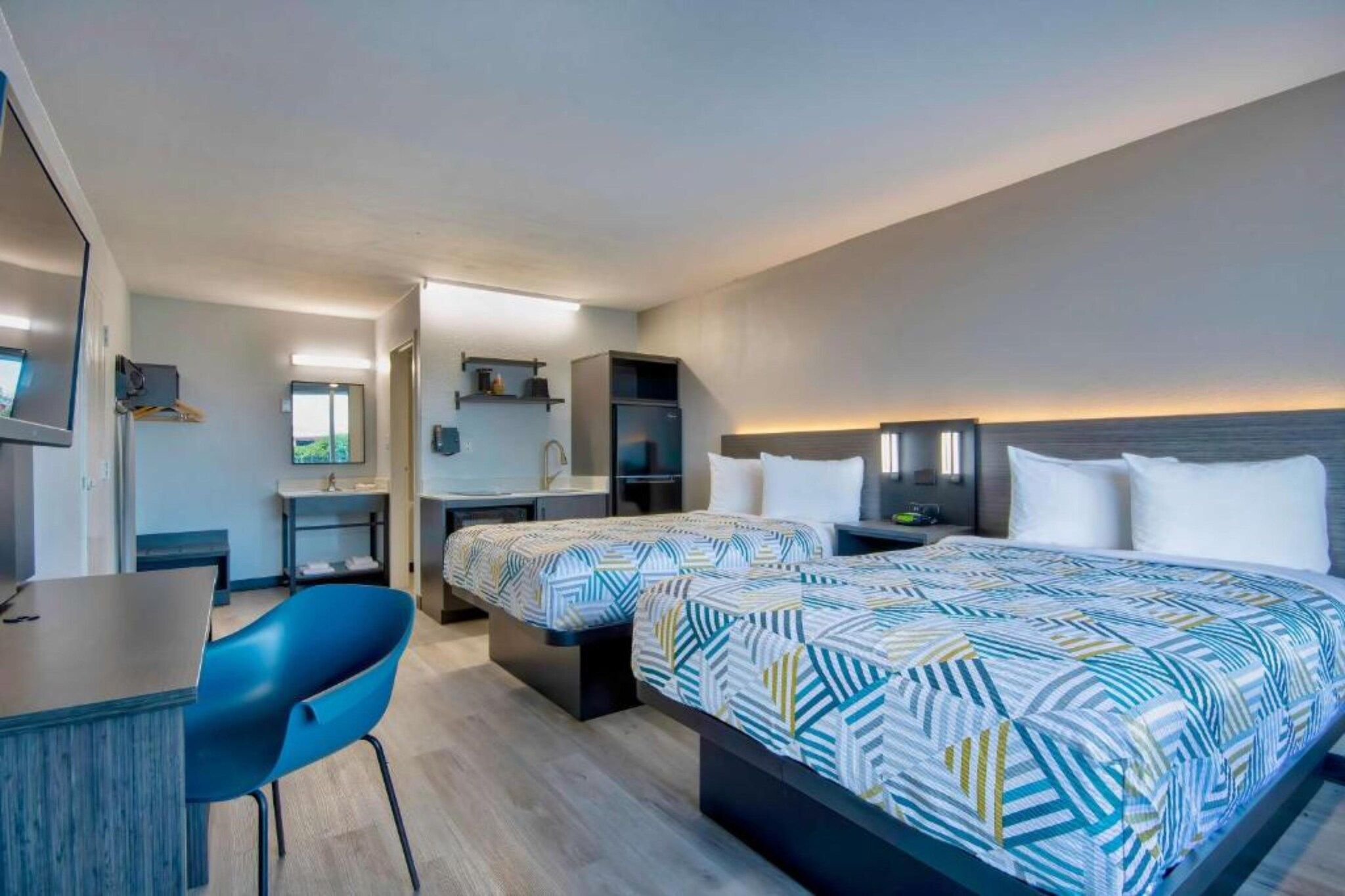 A hotel room with a bed, a desk, a chair, and a television.