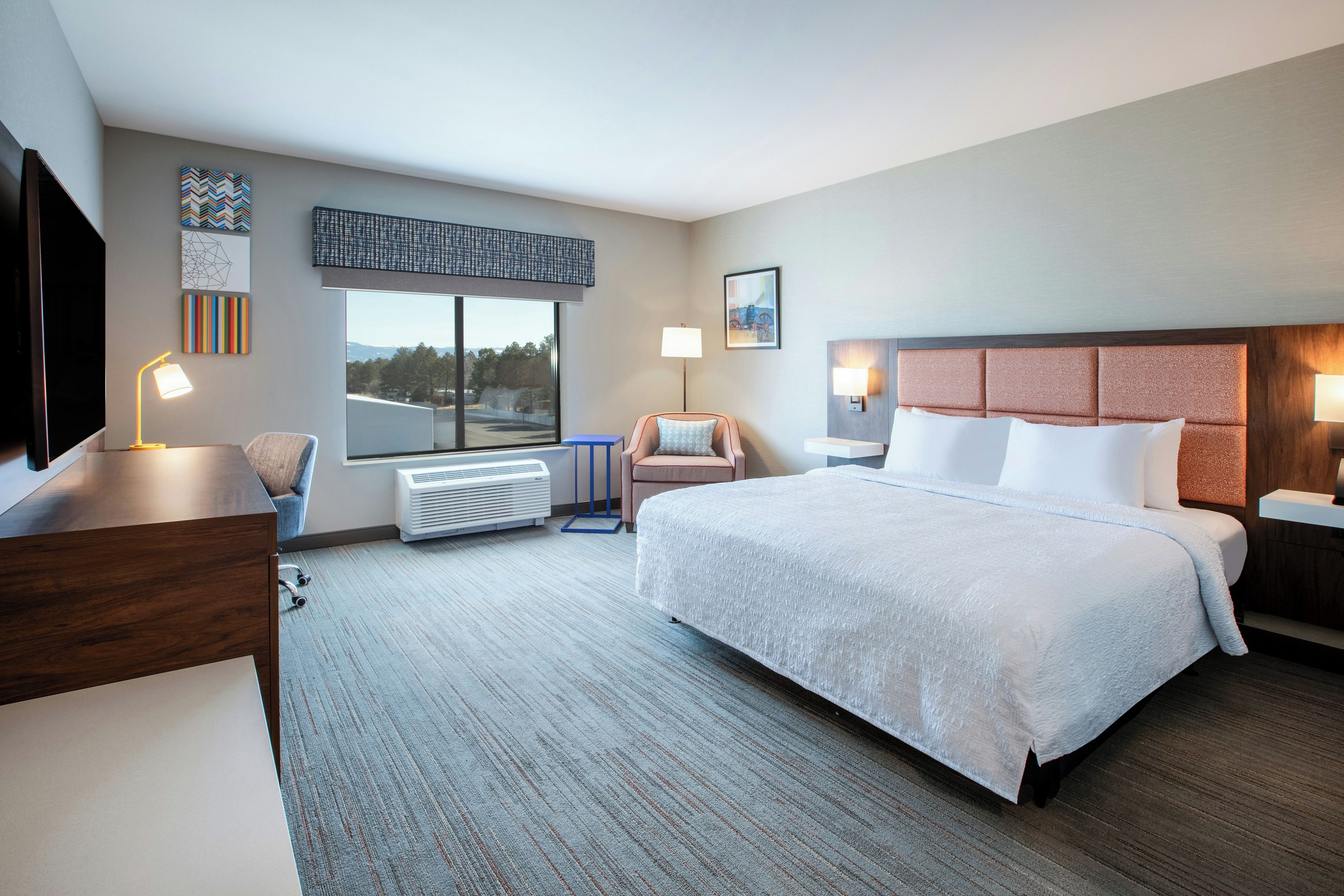 A hotel room with a large bed, a desk, a chair, a window with a view, and a flat-screen TV.