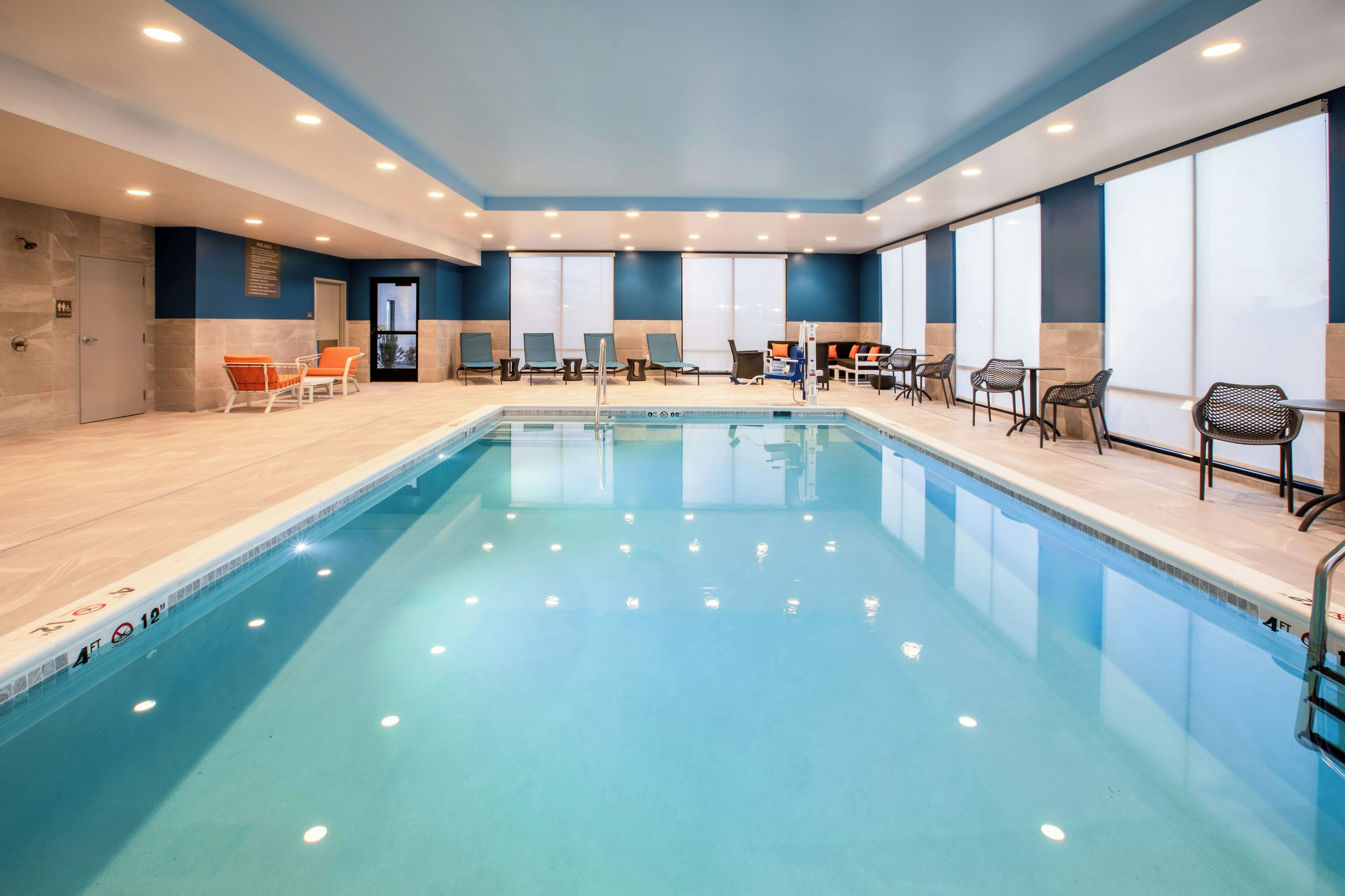 An indoor swimming pool with lounge chairs and tables on the sides.