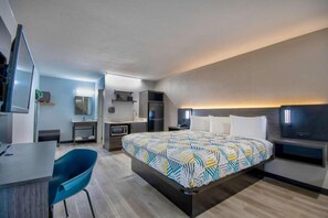Ett modernt hotellrum med en säng, ett skrivbord, en stol, en TV och ett badrum.