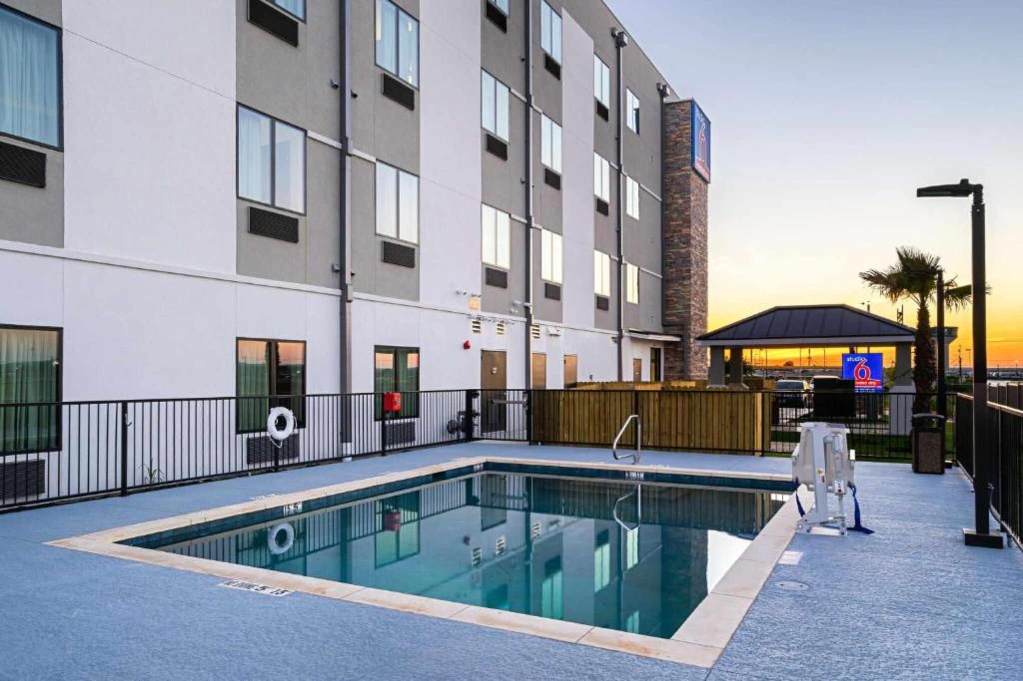 A hotel with a swimming pool, a covered area, and a view of the sunset.