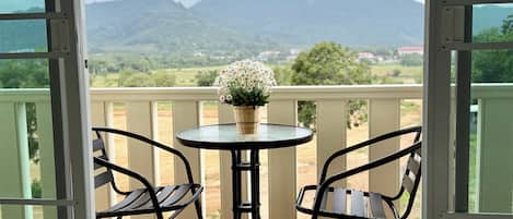 A balcony with a table and chairs, overlooking a mountainous landscape.