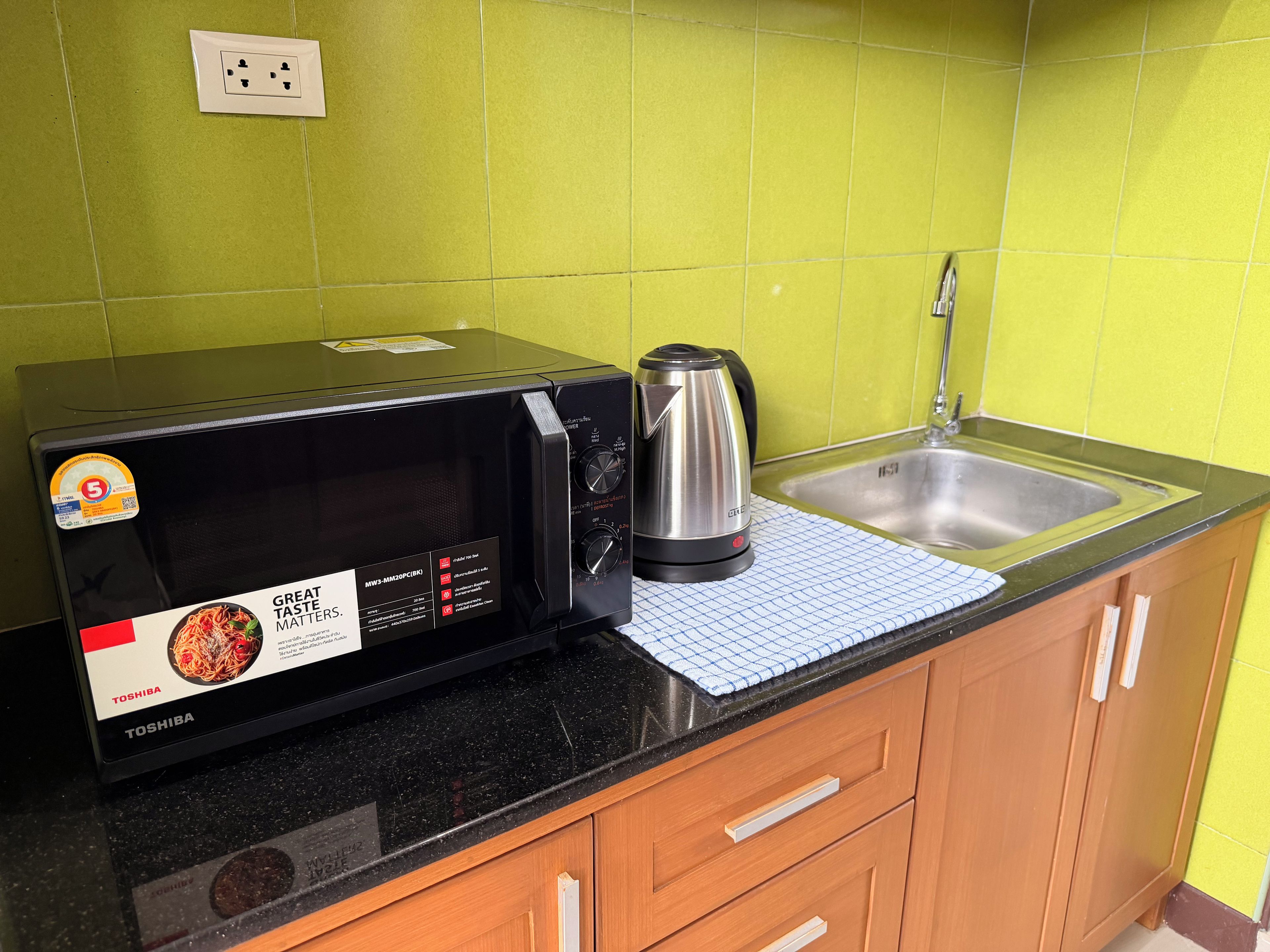 Una cocina con un microondas negro, un hervidor y un lavamanos.