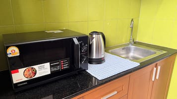 Una cocina con un microondas negro, un hervidor y un lavamanos.