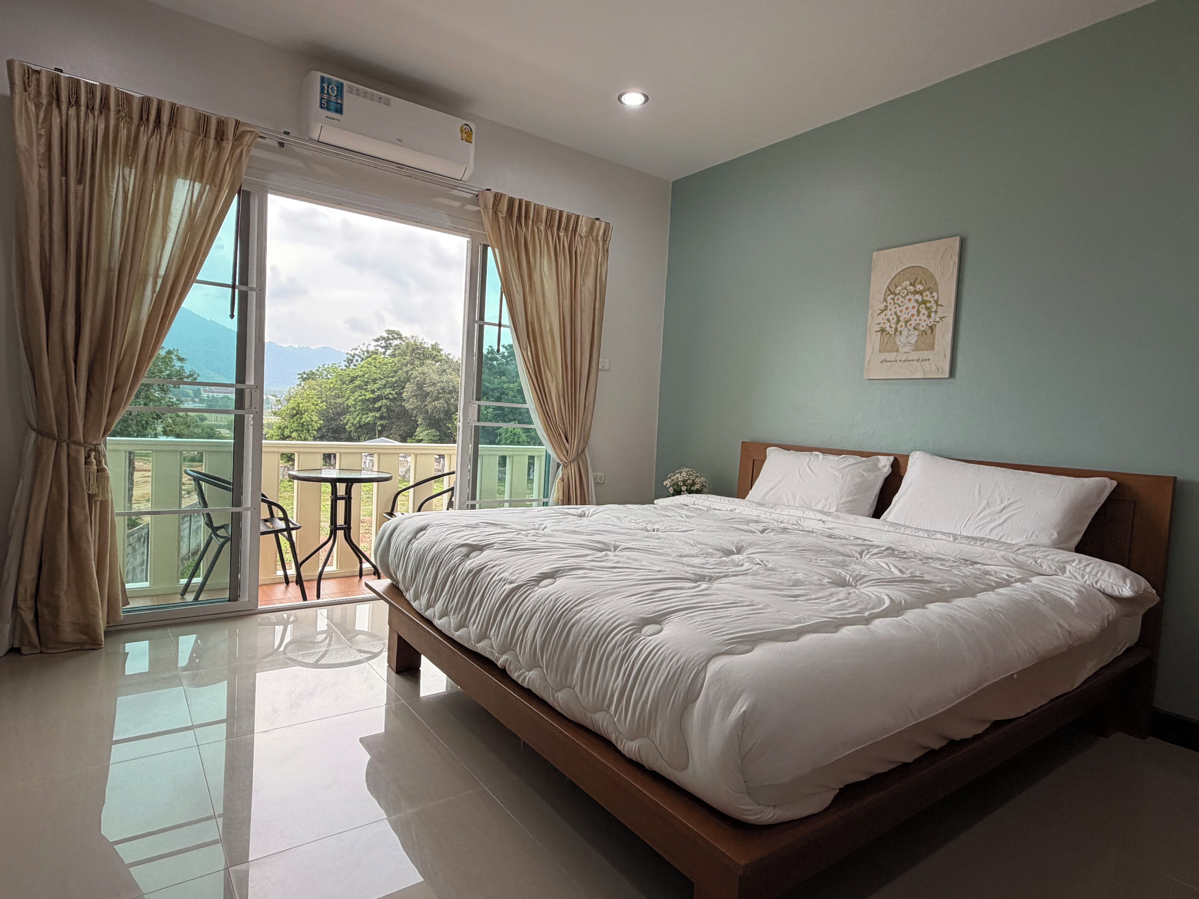 A hotel room with a bed, curtains, a balcony with a table and chairs, and a ceiling-mounted air conditioner.