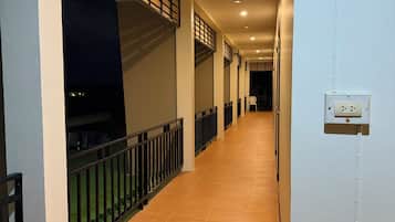 A corridor with a tiled floor, a railing on one side, and a wall-mounted electrical outlet on the other.