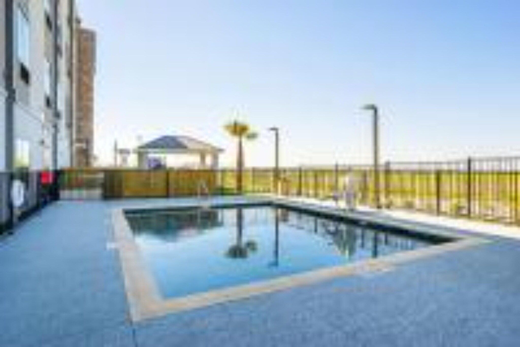 Una piscina con deck azul, una zona de estar cubierta y un edificio al fondo.