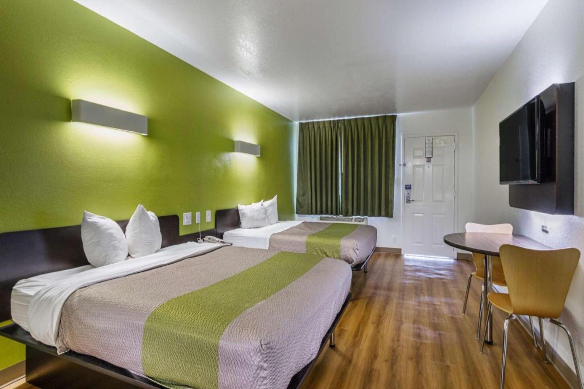 Ein Hotelzimmer mit zwei Betten, einem Schreibtisch, einem Sessel, einem Fernseher und einem Fenster mit Vorhängen.