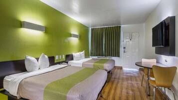 Ein Hotelzimmer mit zwei Betten, einem Schreibtisch, einem Sessel, einem Fernseher und einem Fenster mit Vorhängen.