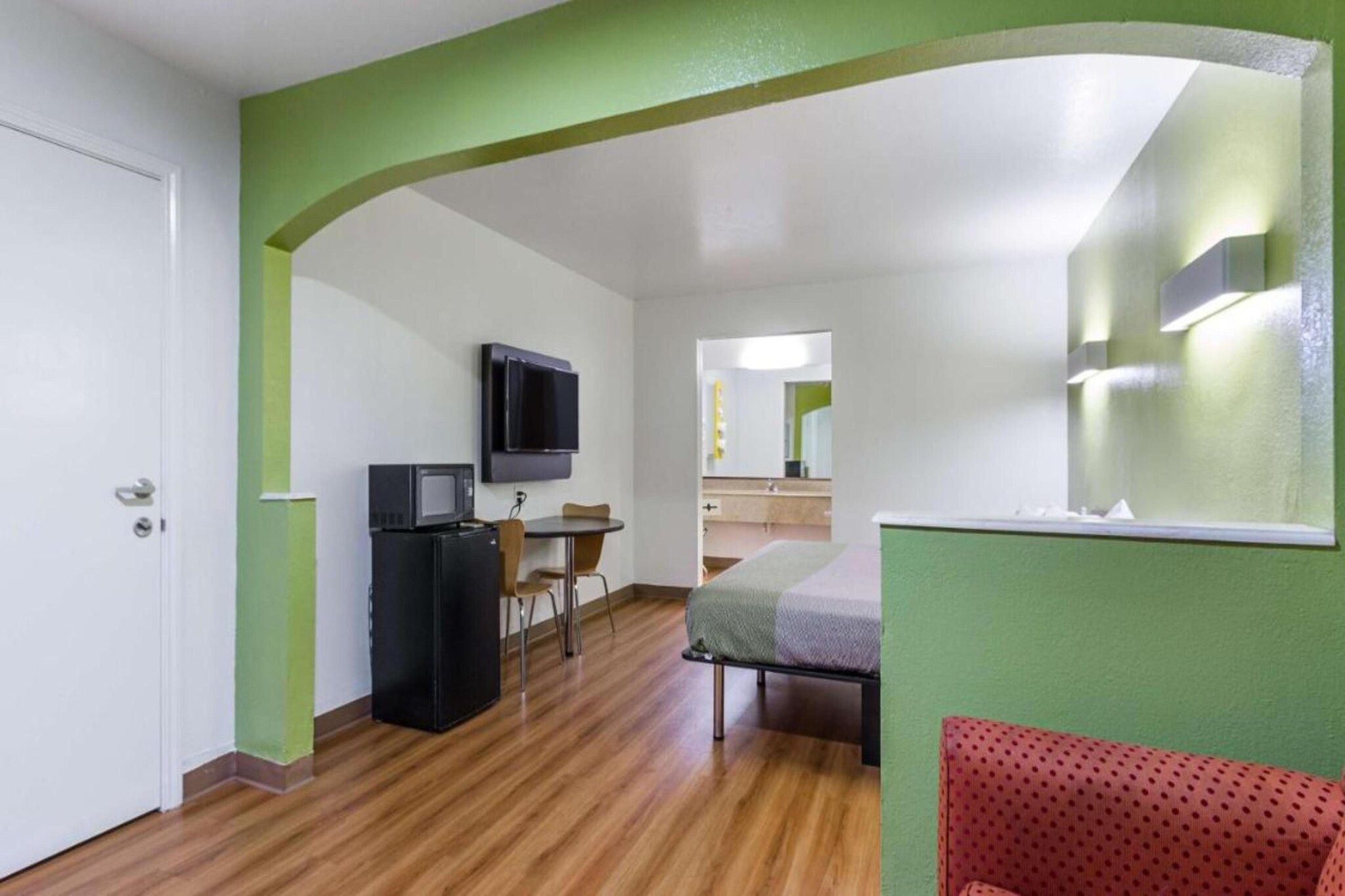 A compact room with a bed, a desk with a chair, a television, and a refrigerator.