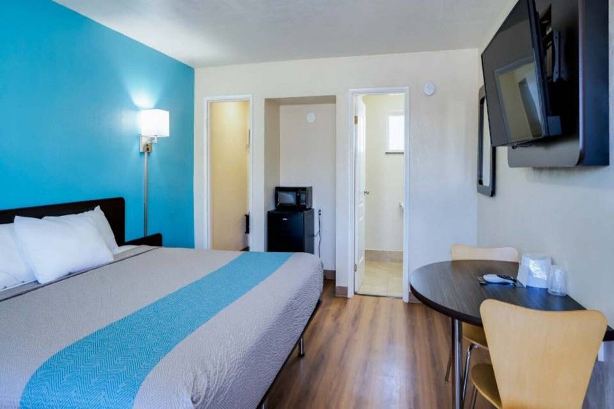 A hotel room with a bed, a desk, a chair, a TV, and a microwave.
