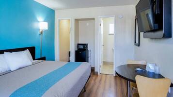A hotel room with a bed, a desk, a chair, a TV, and a microwave.
