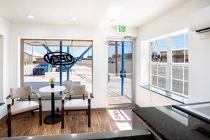 A hotel lobby with a reception desk, two chairs, a small table with a plant, and a view of the parking area through glass doors. - 1 King Bed | Smoking, Micfridge (Odessa TX)