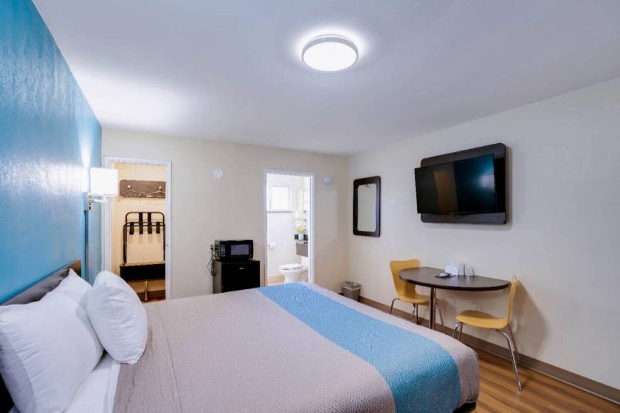 Hotellihuone, jossa on sänky, työpöytä, tuoli, televisio ja kylpyhuone, joka näkyy avoimen oven läpi.