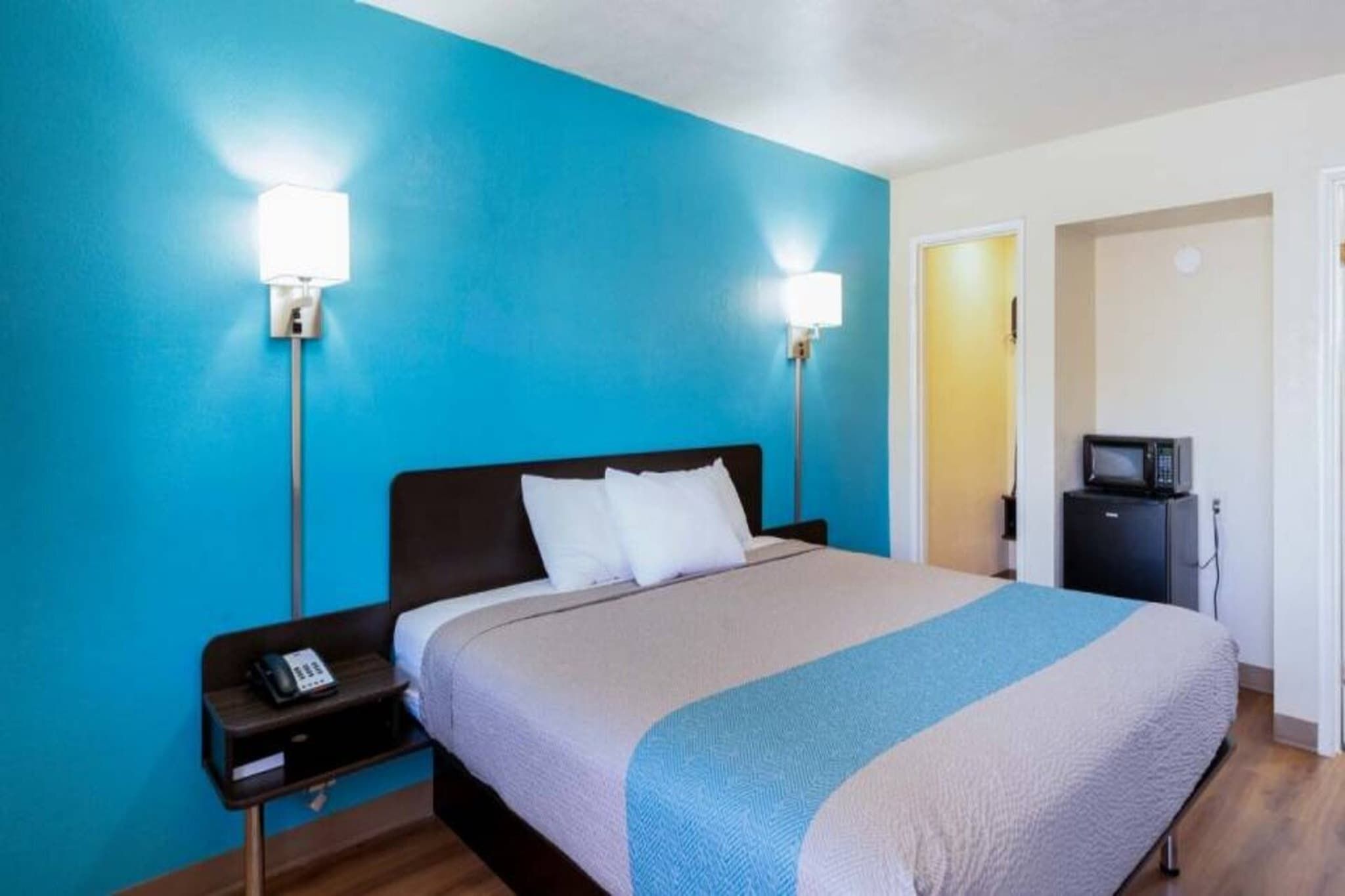 A hotel room with a bed, bedside tables, a telephone, and a microwave.