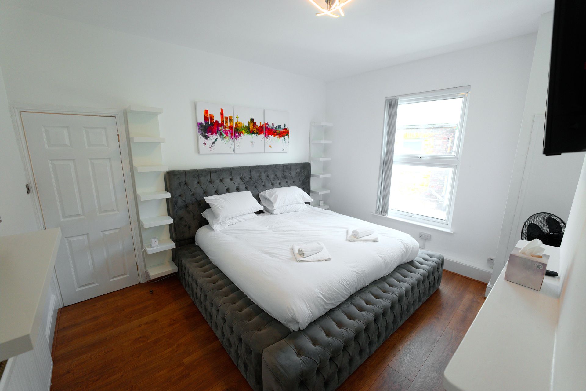 A modern bedroom with a large bed, a window, and a decorative wall piece.