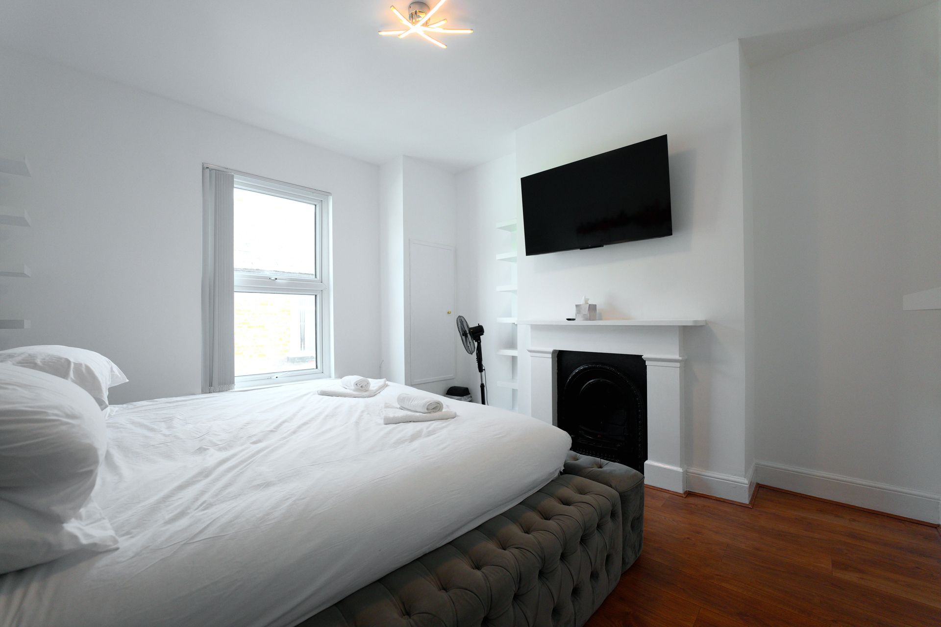 Quarto moderno com cama grande, TV de tela plana instalada acima de uma lareira e janela que proporciona luz natural.