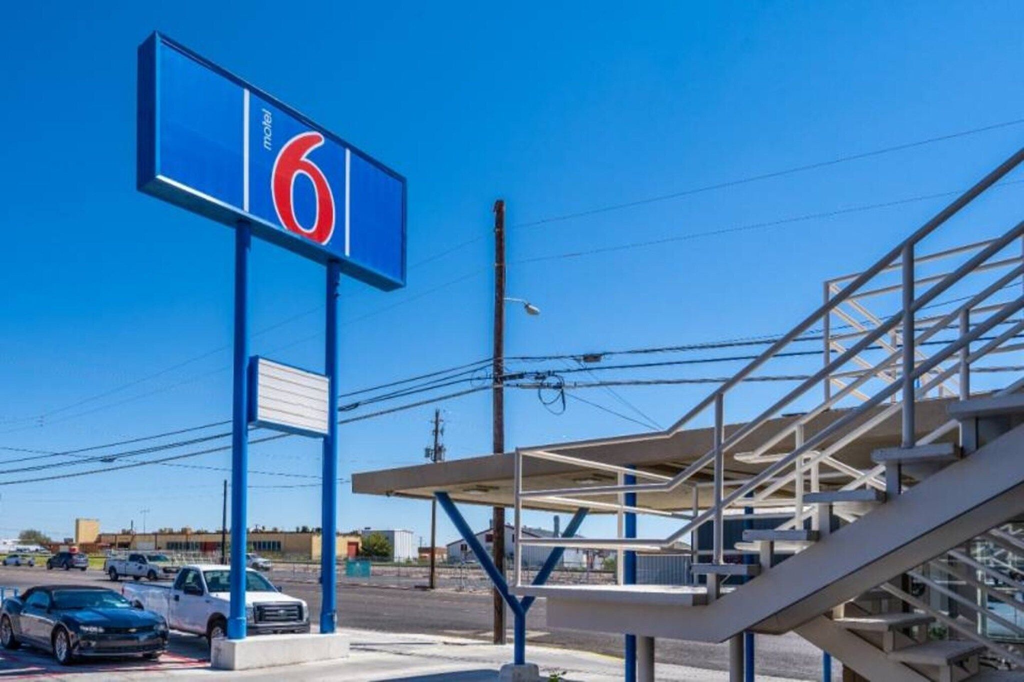 A motel sign with the number 6, a parking lot with several cars, and a building with a staircase.