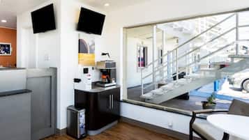 A modern hotel room with a large window, a small kitchenette, a seating area, and a staircase leading to an outdoor area.