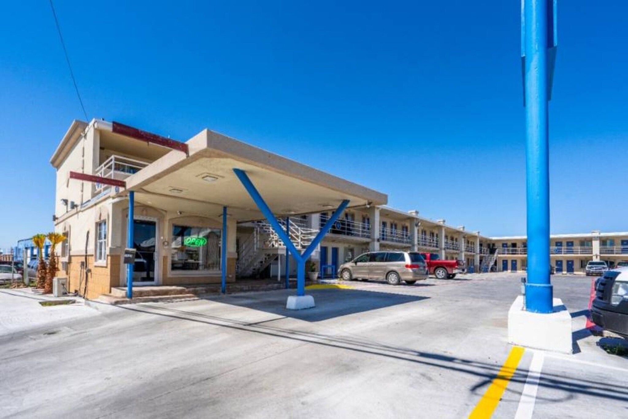 A gas station with a covered fuel pump area, multiple cars parked, and a clear blue sky.