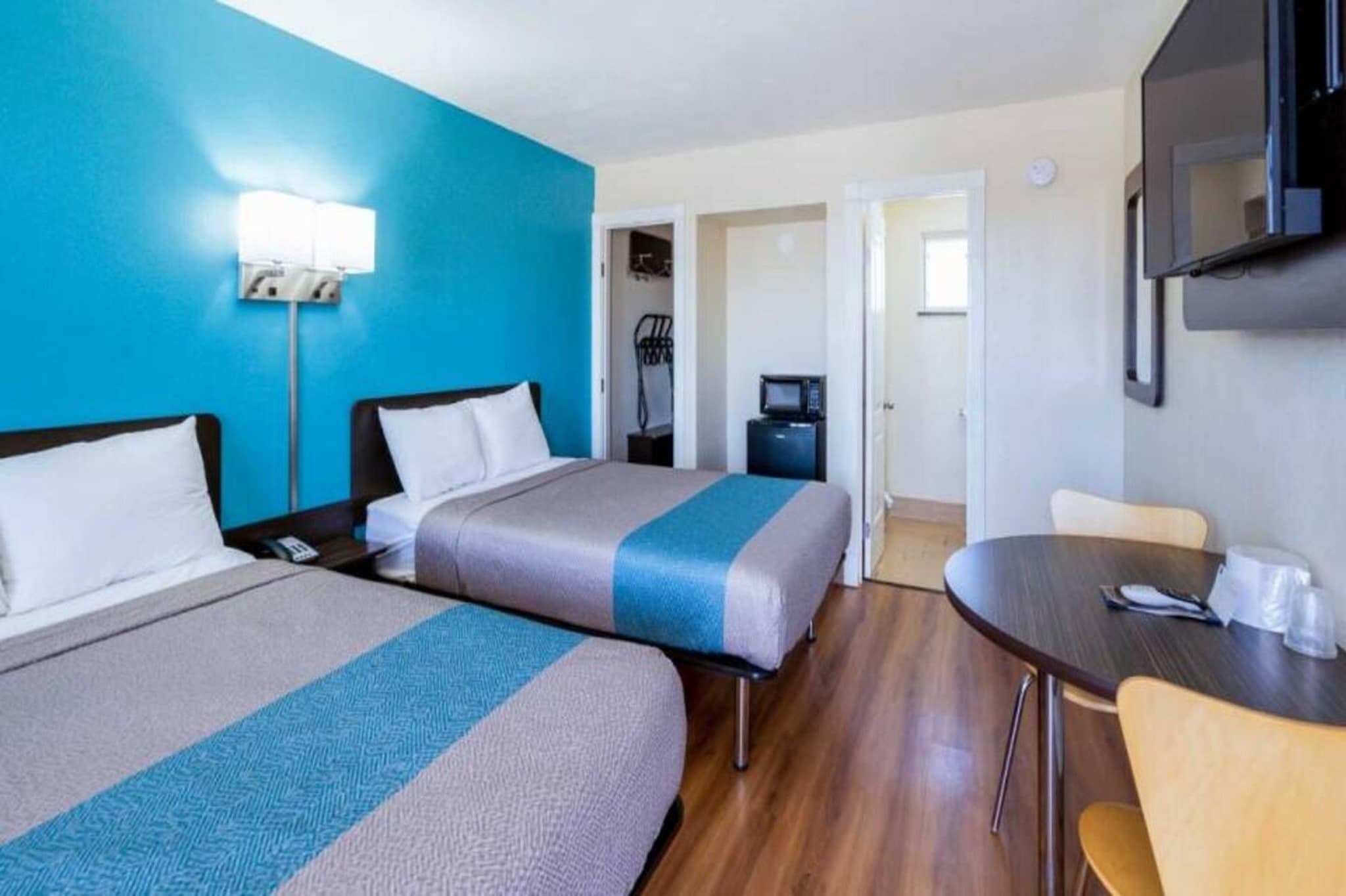 A hotel room with two beds, a desk, a chair, a television, and a door leading to a bathroom.