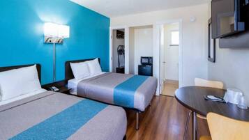 A hotel room with two beds, a desk, a chair, a television, and a door leading to a bathroom.