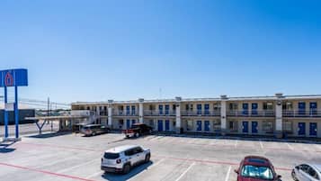 A motel with multiple rooms, a parking lot, and a clear blue sky.