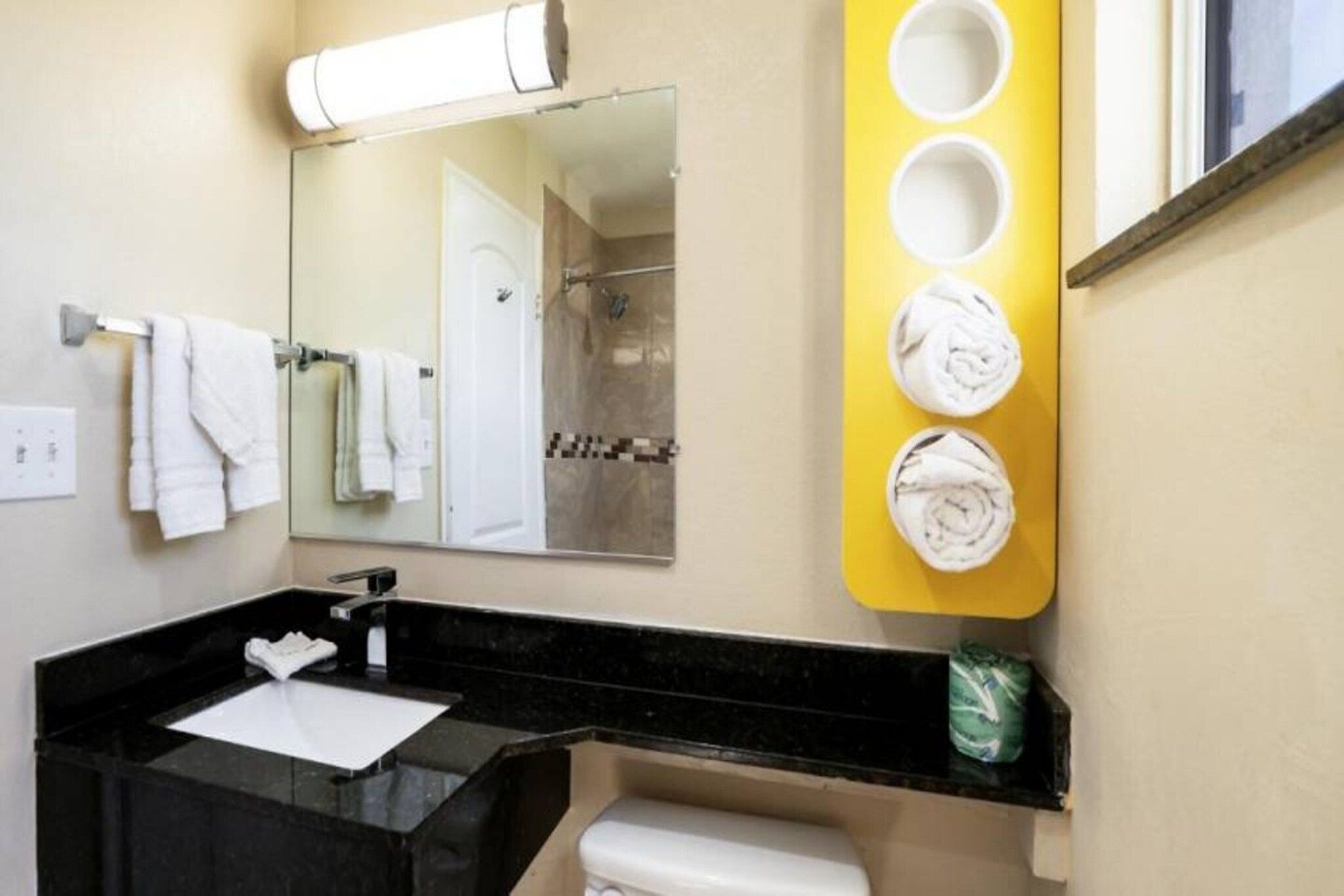 A bathroom with a black sink, white toilet, and a mirror above the sink. There are towels hanging on a rack and a yellow towel warmer with towels on it.
