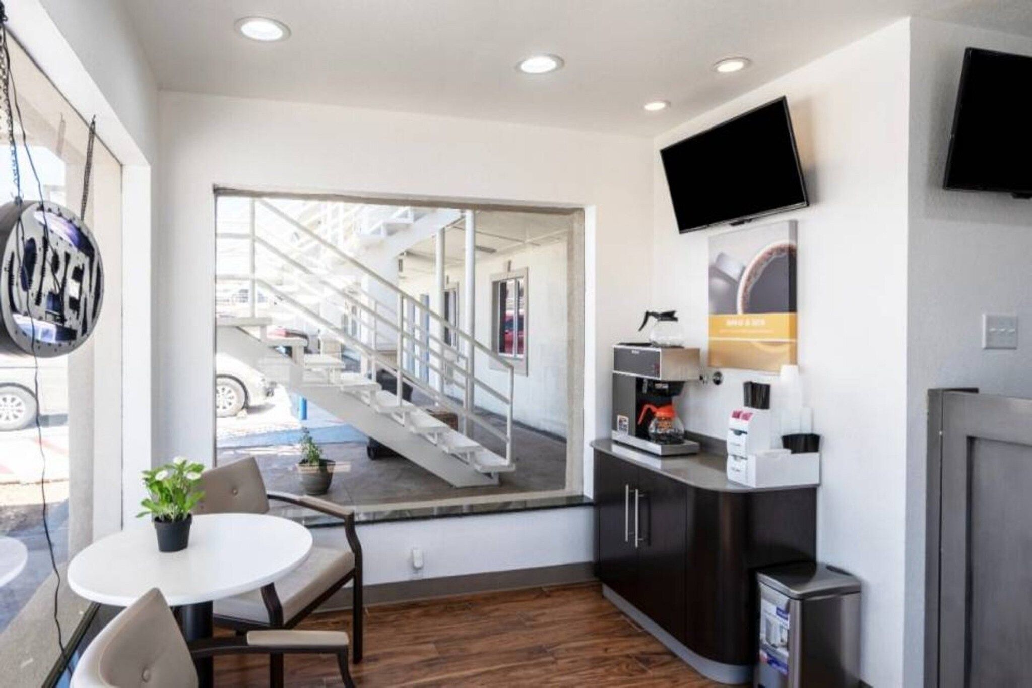 A modern hotel room with a large window, a flat-screen TV, a coffee machine, and a small table with a chair.
