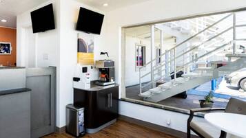 A modern hotel room with a large window, a small kitchenette, a seating area, and a staircase leading to an outdoor area.