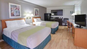 Een hotelkamer met twee bedden, een bureau, een stoel, een televisie en een kitchenette.