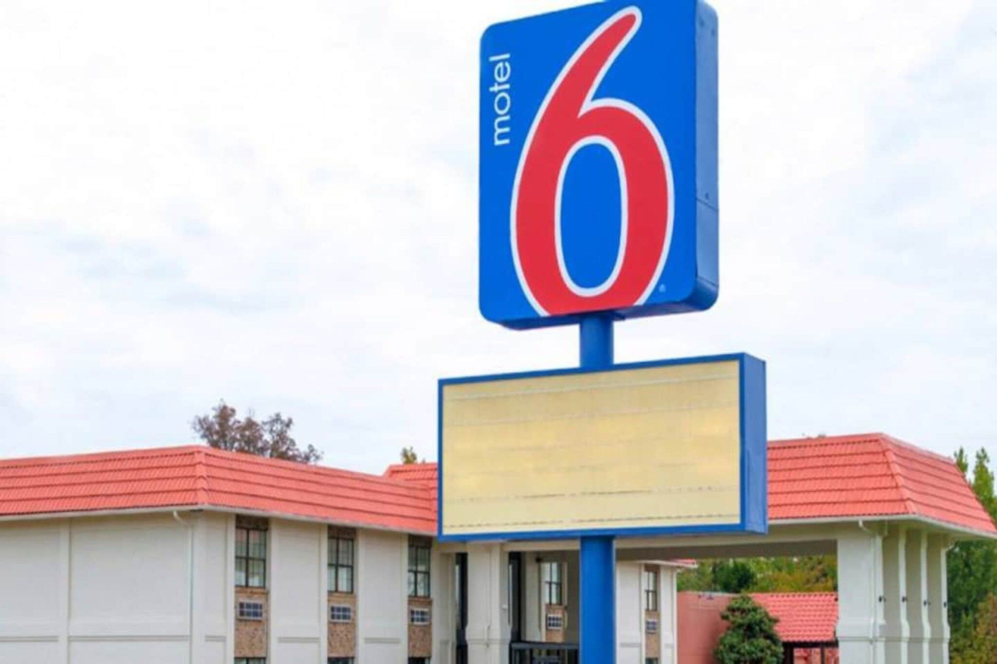 Un panneau indiquant un motel avec le chiffre 6, un bâtiment doté d’un toit rouge et un panneau d’affichage vierge.