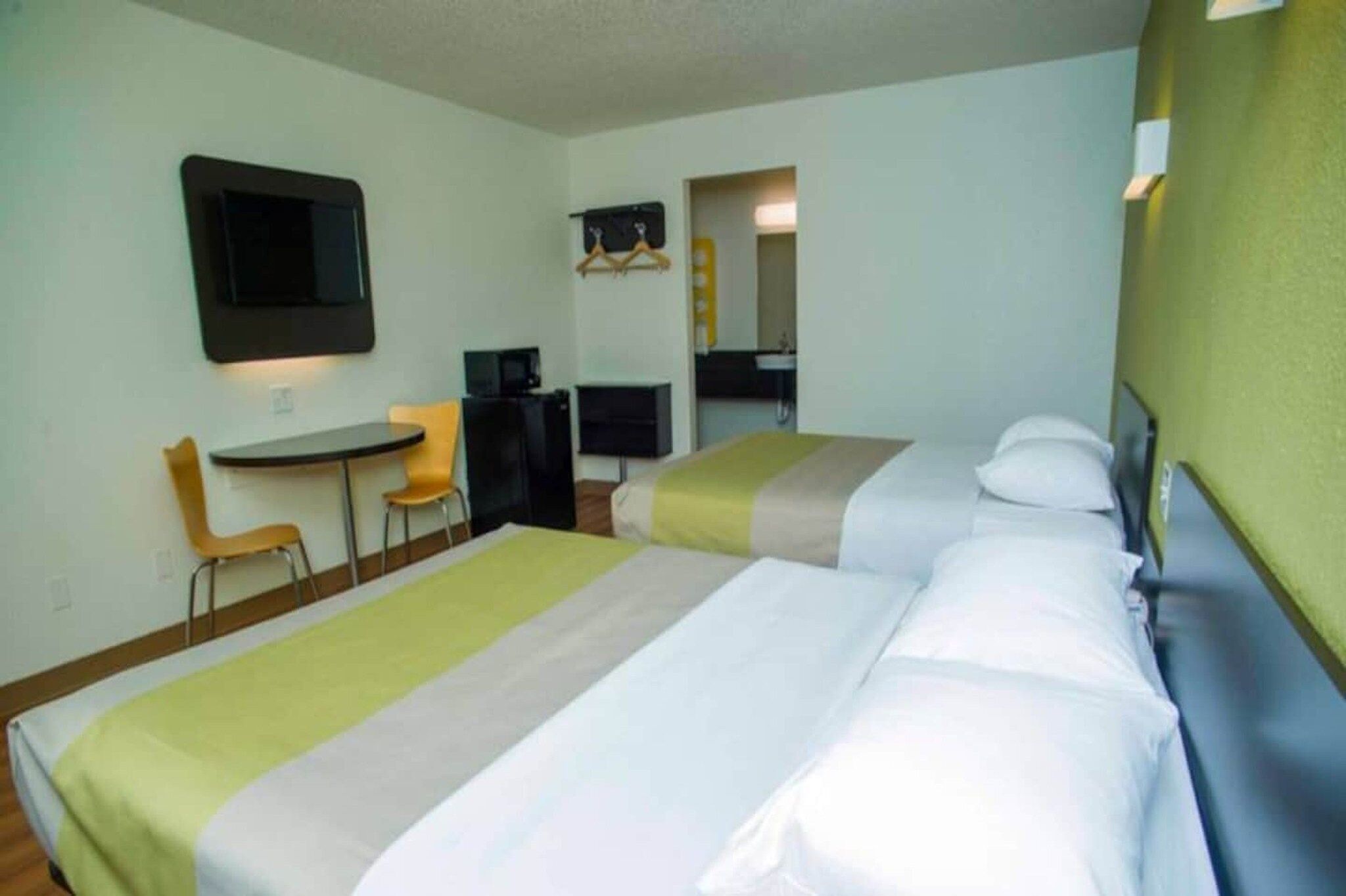 A hotel room with two beds, a desk, a chair, a television, and a bathroom visible through an open door.