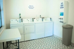 Ein Waschraum mit Tisch, vier Waschmaschinen, einem Mülleimer und einem Schild an der Wand.