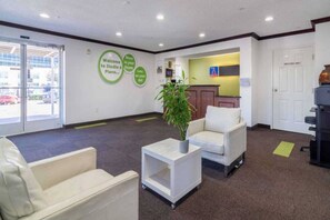 Un espace d’accueil comprenant un comptoir de réception, deux chaises blanches, une petite table avec une plante et un panneau orné de motifs circulaires verts.