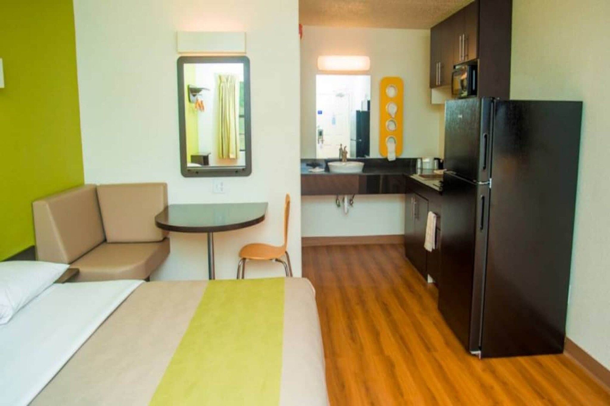 Habitación de hotel con cama, una pequeña mesa, sofá, kitchenette con refrigerador y un espejo.
