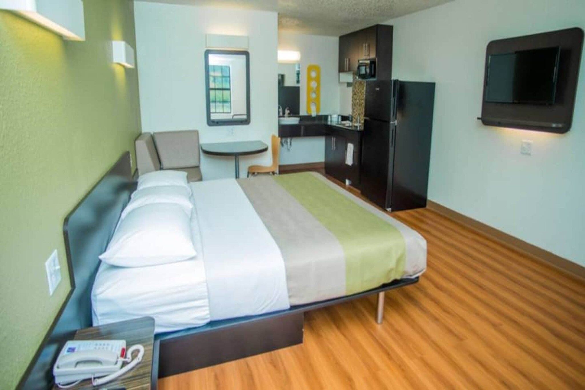 Una camera d'albergo con un letto, una scrivania, una sedia, un angolo cottura e una TV.