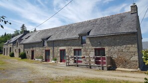 A stone building with multiple windows and doors, a gravel driveway, and a small porch area. - Holiday Home 'Ty Prawine' with Terrace, Garden and Wi-Fi (Quistinic)