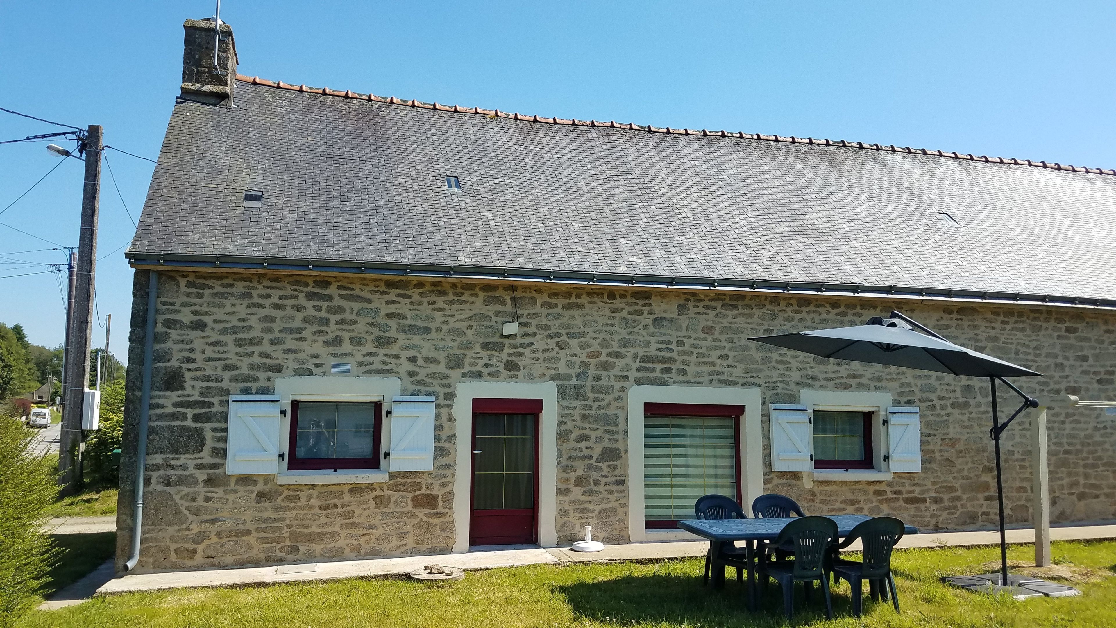 A stone building with a tiled roof, a red door, and a table with chairs outside.