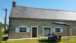 A stone building with a tiled roof, a red door, and a table with chairs outside. - Holiday Home 'Ty Prawine' with Terrace, Garden and Wi-Fi (Quistinic)