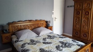 A bed with a patterned bedspread, a wooden headboard with carvings, bedside lamps, and a wardrobe with decorative panels. - Holiday Home 'Ty Prawine' with Terrace, Garden and Wi-Fi (Quistinic)