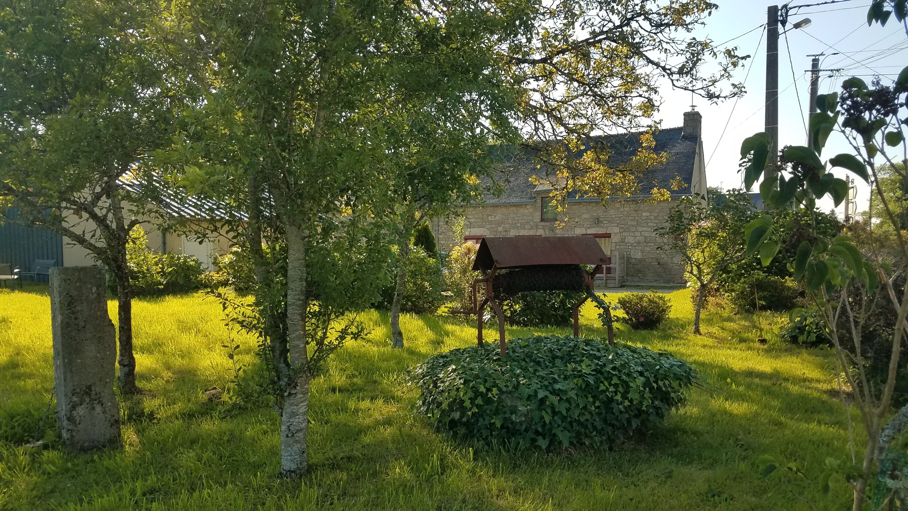 A grassy area with a stone building, a metal structure, and trees.