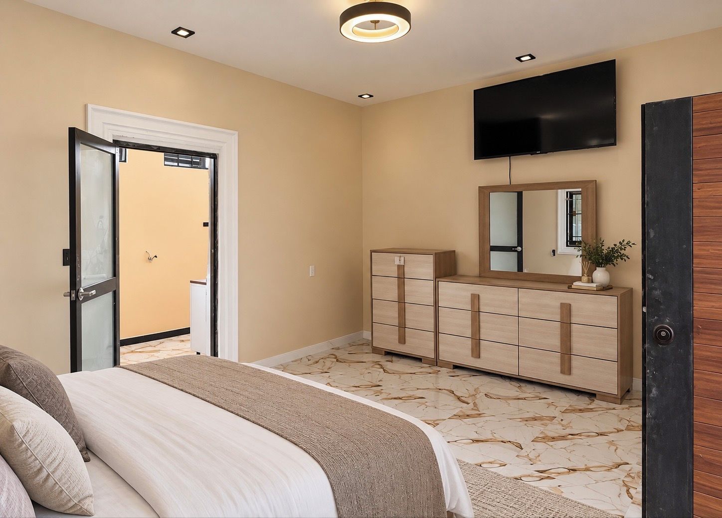 Een slaapkamer met een bed, een dressoir, een spiegel en een televisie aan de muur.