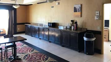 Een hotelkamer met een keukenhoek, met donkere kastjes, een magnetron en een koffiezetapparaat op het aanrecht.