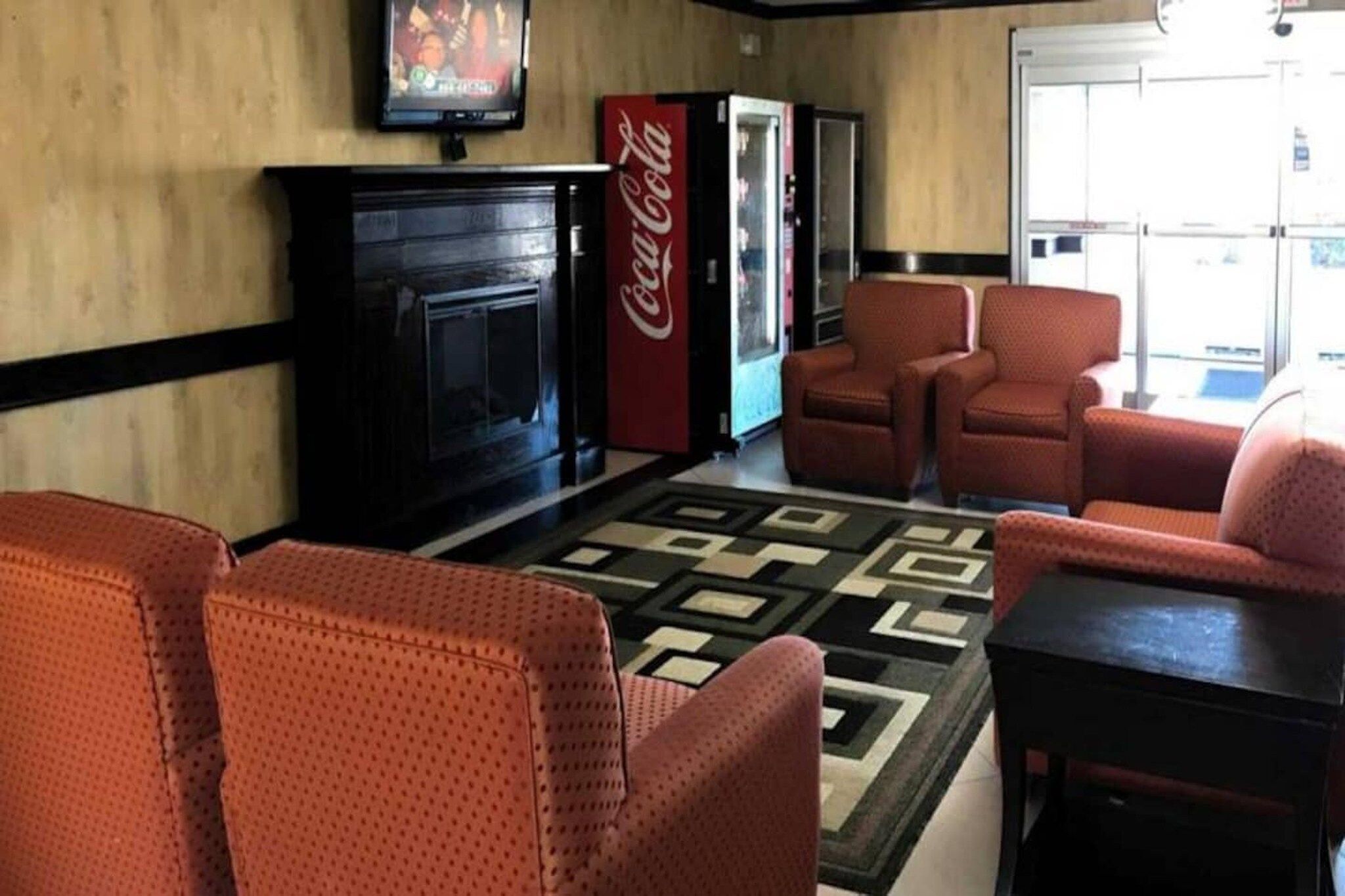 A lobby with a fireplace, red armchairs, a patterned rug, and a Coca-Cola refrigerator.