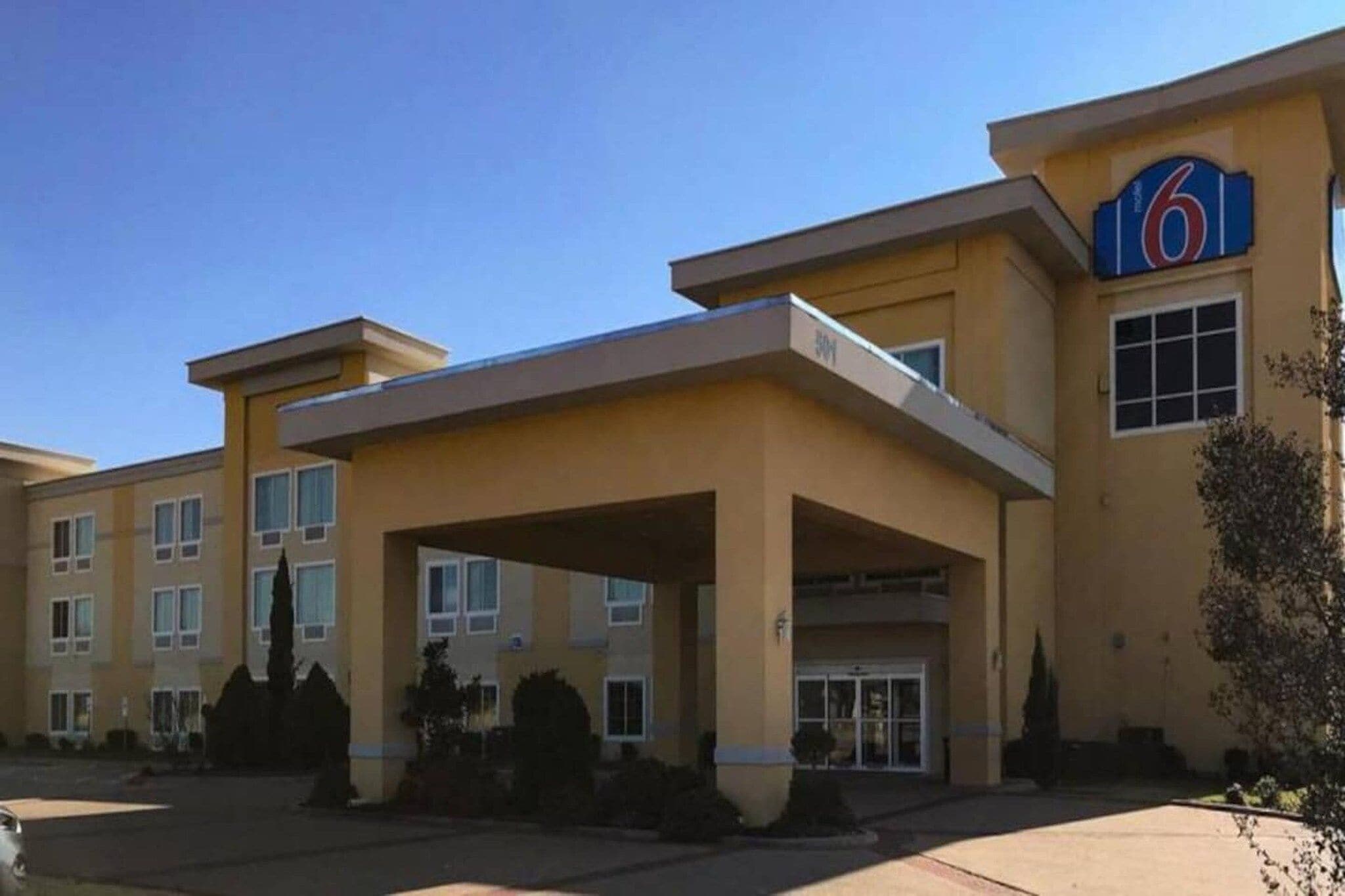 A multi-story hotel with a prominent '6' sign, a covered entrance, and a parking lot.