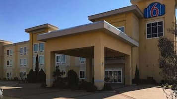 A multi-story hotel with a prominent '6' sign, a covered entrance, and a parking lot.