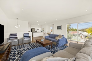 A modern living room with a sofa, armchairs, a coffee table, and a TV. - Coral Haven ~ Port Willunga - Seaside Sanctuary in a Prime Port Willunga Location (Port Willunga)