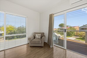 A room with a beige armchair, a large sliding glass door, and a view of a residential area. - Coral Haven ~ Port Willunga - Seaside Sanctuary in a Prime Port Willunga Location (Port Willunga)