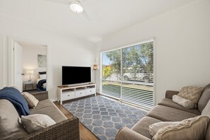 A living room with a flat-screen TV, a sofa, a coffee table, and a patterned rug. - Coral Haven ~ Port Willunga - Seaside Sanctuary in a Prime Port Willunga Location (Port Willunga)